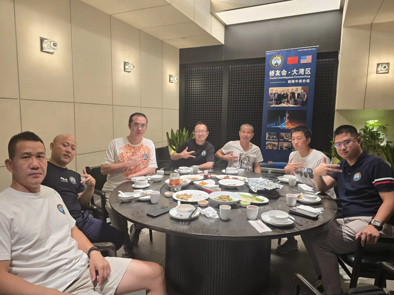 彩虹桥 9/5 广州番禺桥友会:七位桥友在桥友宴圆桌前合影,身后是桥友会·大湾区易拉宝